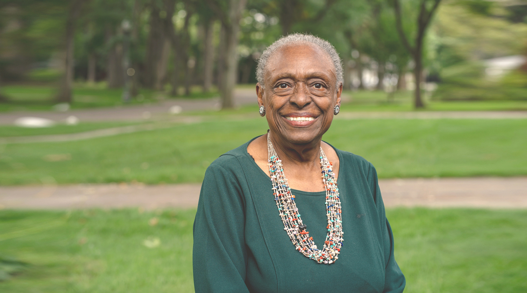 Doctor Glenda Price, an older Black woman, smiles with trees and grass in the background